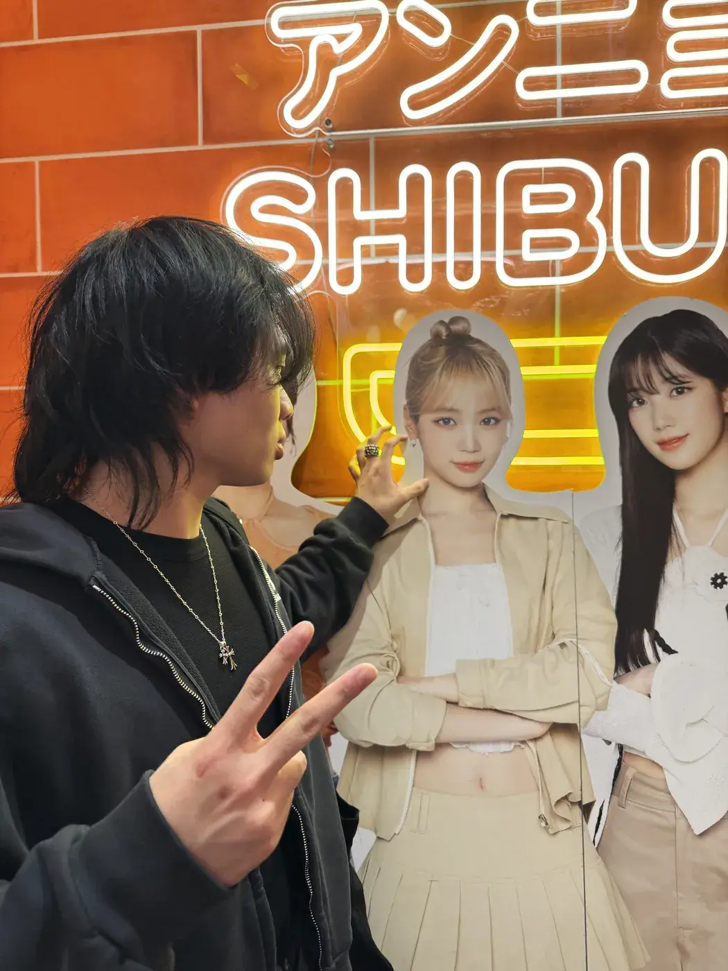 Elliot making a peace sign beside a Shibuya shop sign