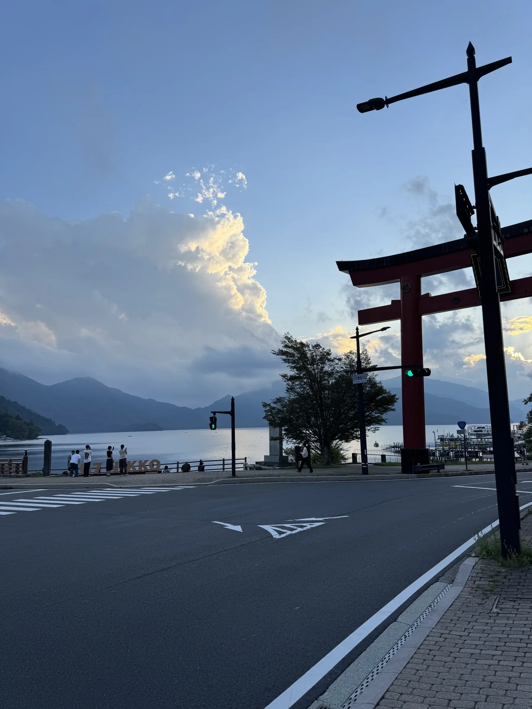 A quiet road beside a lake in Japan, with a torii gate and mountains beyond